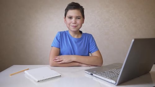 Boy Smiles at Desk with Computer and Notebook