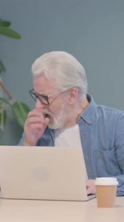 Senior Man Coughing While Working on Laptop