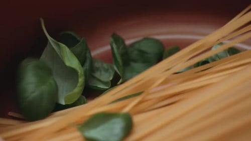 Basilikumblätter in einen Kupfertopf mit ungekochten Linguine-Spaghetti-Nudeln geben. Schuss aus der Hand. Nahaufnahme.