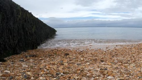 Cristal clear water waves gently kissing the orange pebble beach in the Isle of Wight. Steady camera