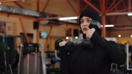 Athletic Woman Doing Dumbbell Front Raises in Gym