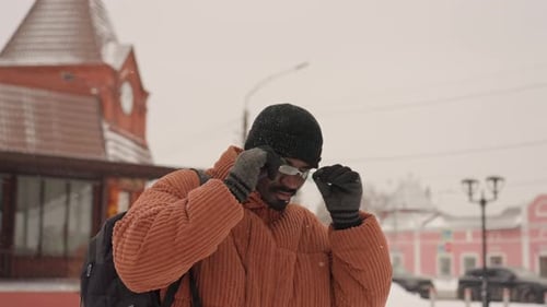 Smiling Man Removing Glasses on Snowy City Street