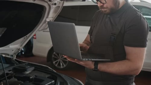Car Service Technician Typing on Laptop while Diagnosing Engine Performance