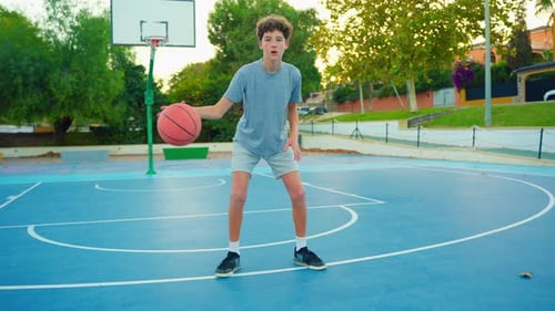 Curly Young Sportsman Posing with Ball in Sunlight on Outdoor Court A Young Man Hits the Ball