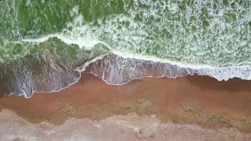 Aerial View of Ocean Waves Crashing Onto a Sandy Beach Creating a Beautiful Contrast Between the