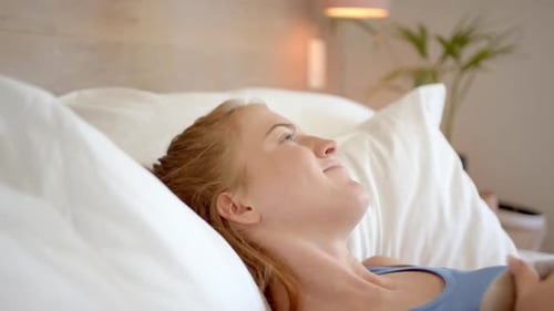 Détente au lit, femme allongée sur des oreillers et levant les yeux, se sentant en paix