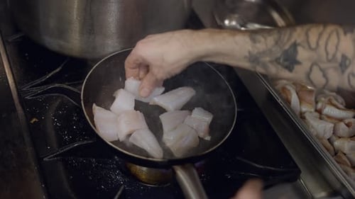 Close View of Tattooed Male Chef Placing White Fish in Frying Pan