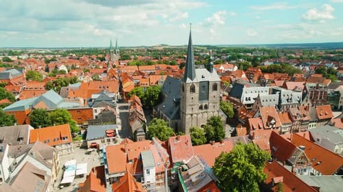 Historic European townscape with red-tiled roofs and medieval church spires under blue summer sky