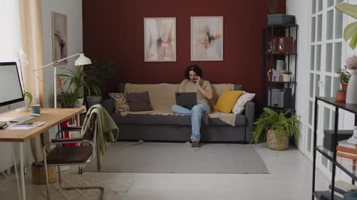 Man on Couch Using Laptop and Talking on Phone