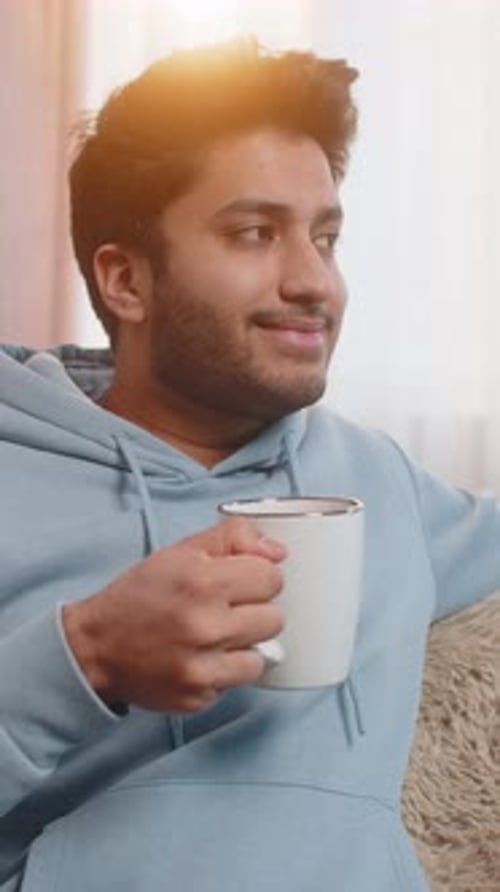 Young man drinking coffee indoors in bright sunlight