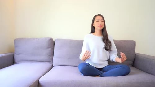 Young Woman Meditating Peacefully on Sofa at Home
