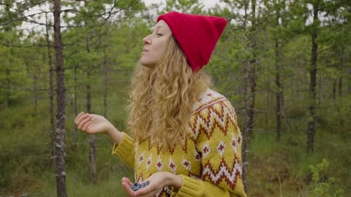 Young Woman in Hat Tastes Collected Wild Berries in Forest