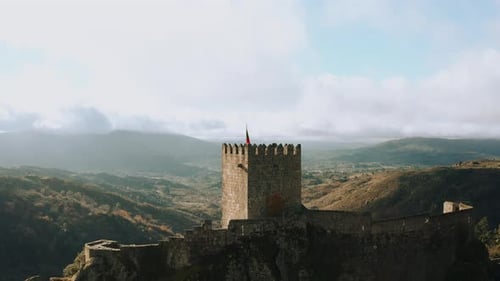 Medieval historical castle turret with flag overlooking deep canyon, aerial dolly in
