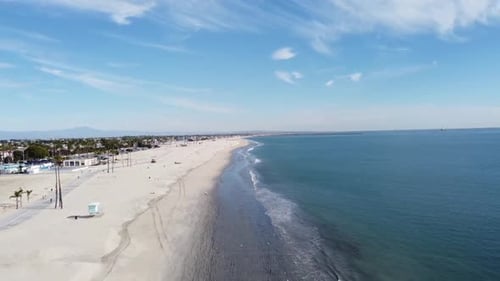Drone flies in from ocean over beach, bike path and parking lot.