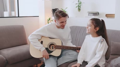 Man Playing Guitar for a Smiling Girl at Home