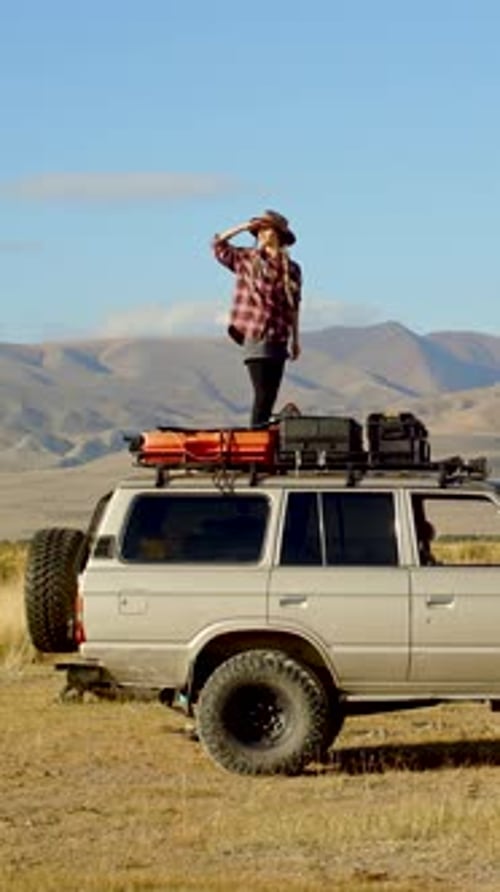 Woman Standing on Overland Vehicle in Rural Setting