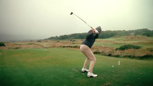 Male golfer hits golf ball with driver off tee on tee box on foggy day on Ireland links golf course