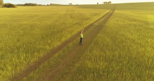 Sporty Child Standing in Green Wheat Field with Raised Hands Up