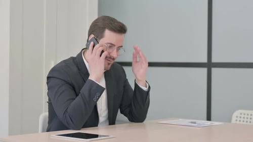 Angry Businessman Talking on Smartphone at Work