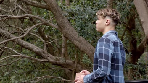 Young man holding coffee cup, enjoying peaceful moment in forest