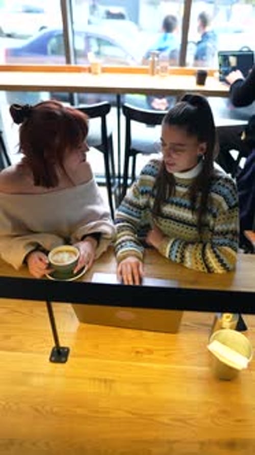 Young Female Friends Working Together with Laptop Computer at Outdoor Cafe