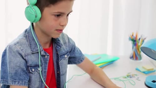 Boy with Headphones Uses Laptop Indoors at Desk