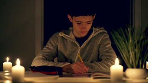 Teen Doing Homework by Candlelight at Night