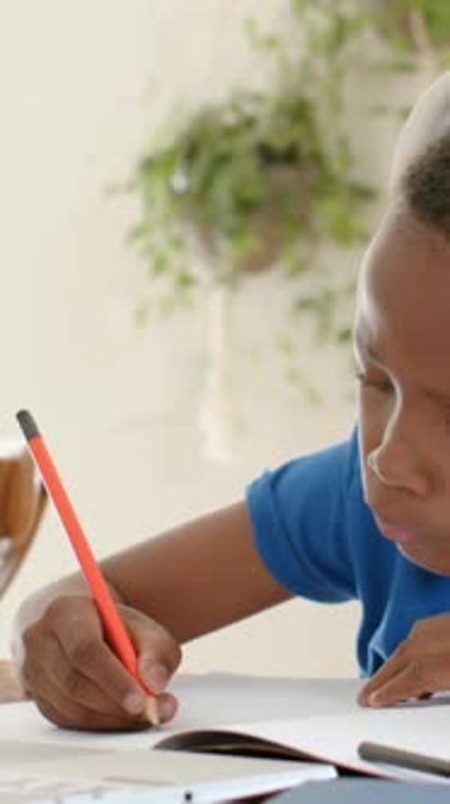 Vertical video: Writing boy in blue tee with red pencil home, pausing, donning headset, copy space