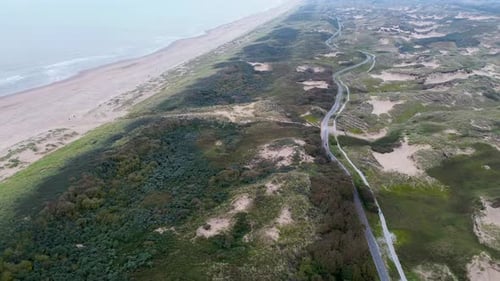 Aerial view of a coastal landscape with lush greenery sandy dunes and winding road running parallel