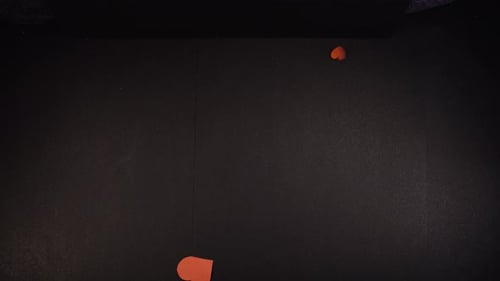 Heart shaped red papers falling on black table, Woman's hands in shot. Above shot with the Sony a7ii