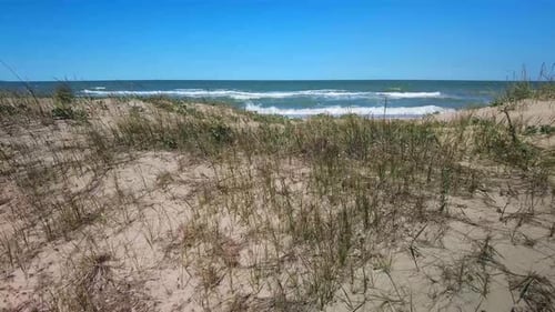 Sea in sunny weather behind a sand dune with grass