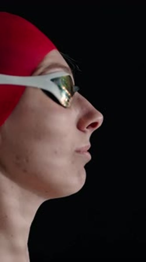 Focused Swimmer in Red Cap and Reflective Goggles Preparing to Compete Captured in Dramatic Side