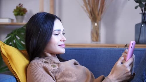 Woman Relaxes on Sofa with Phone and Card