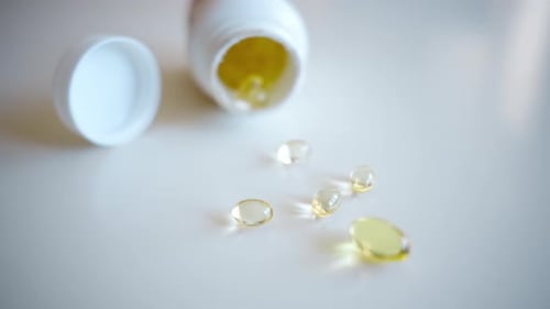 Fish oil omega 3 supplements spilling out of a packer bottle on a white background