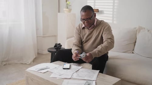 Man Counting Money and Looking at Financial Papers