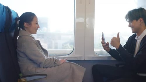 Young Couple Laughing on a Train Using Phone