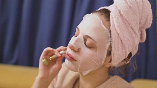 Young Woman Using Jade Roller with Face Mask