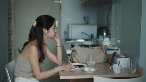 Asian Woman Having Breakfast While Watching Something on a Tablet in a Modern Kitchen