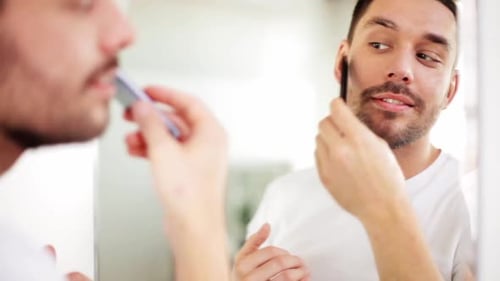 Man Combs and Styles Beard in Bathroom Mirror