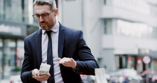 4k video footage of well dressed corporate businessman flicking money away while walking in the city