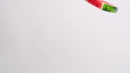 Fresh, bright pink watermelon sliced wedges with green rind raining down on white backdrop in slow m