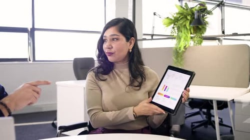 Hispanische Frau im mittleren Erwachsenenalter beim Meeting, hebt Tablet, zeigt Diagramme und präsentiert dann Bericht