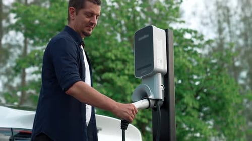 Man recharging battery for electric car during road trip. Exalt