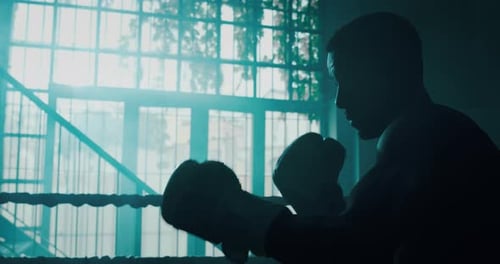 Silhouetted Boxer Practices Punches in Boxing Ring