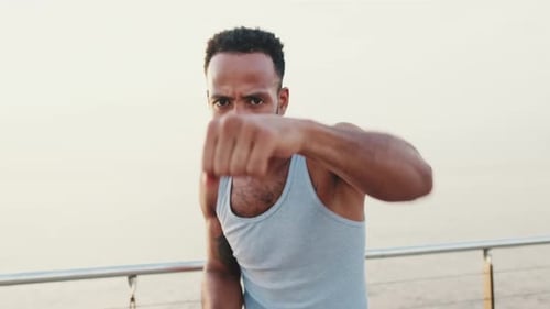 Close up, young fit athlete boxer practicing punching technique while standing on the embankment