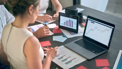 Three people are working and talking in the office. Gadgets and papers with graphs and information