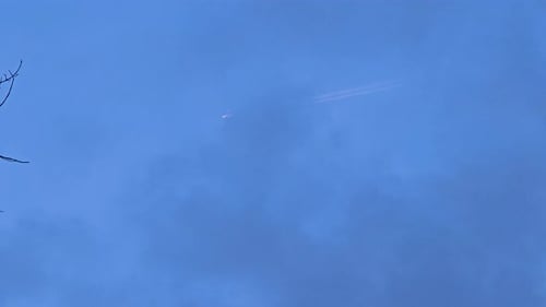 An airplane streaks through the clear blue sky, leaving a contrail behind as it flies above the silh