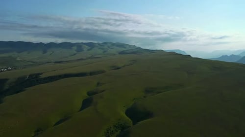 Aerial View of a Green Mountain Range with a Sky Background and Clouds in the Distance