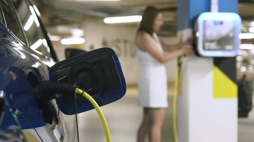 Woman Connects Charging Cable of Electric Vehicle to Point