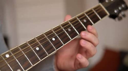 Hand plays guitar chords on fretboard close up